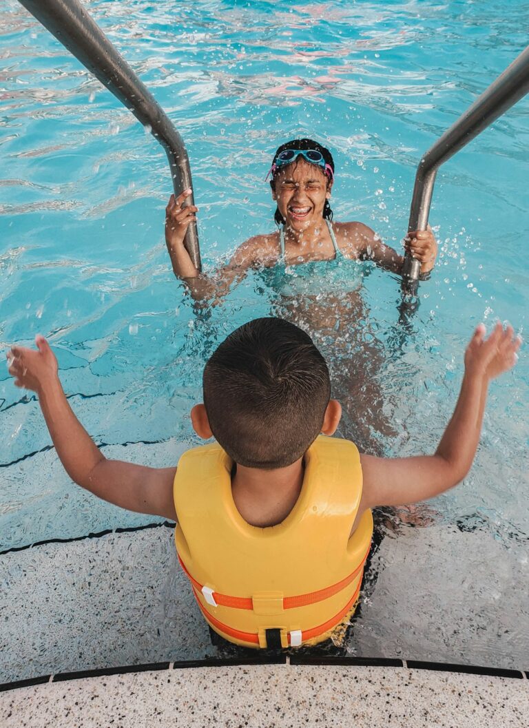 A swim instructor supports a young child learning to float in a warm indoor pool.