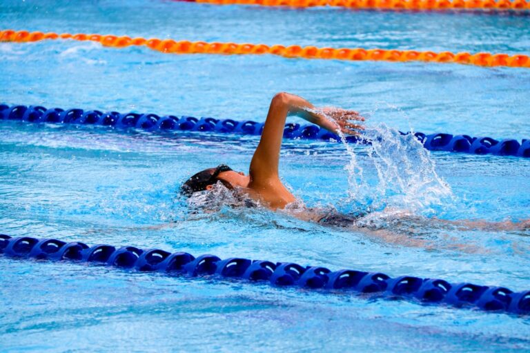 A swim instructor guiding a young child in the water during a swim lesson, both smiling and engaged.