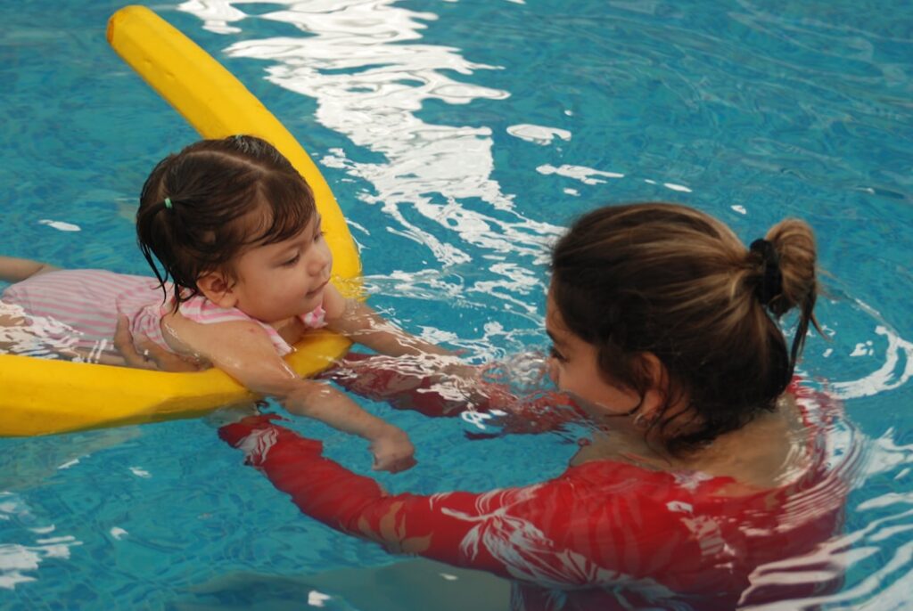 A swim instructor guiding a young child through a gentle water activity in an indoor pool.